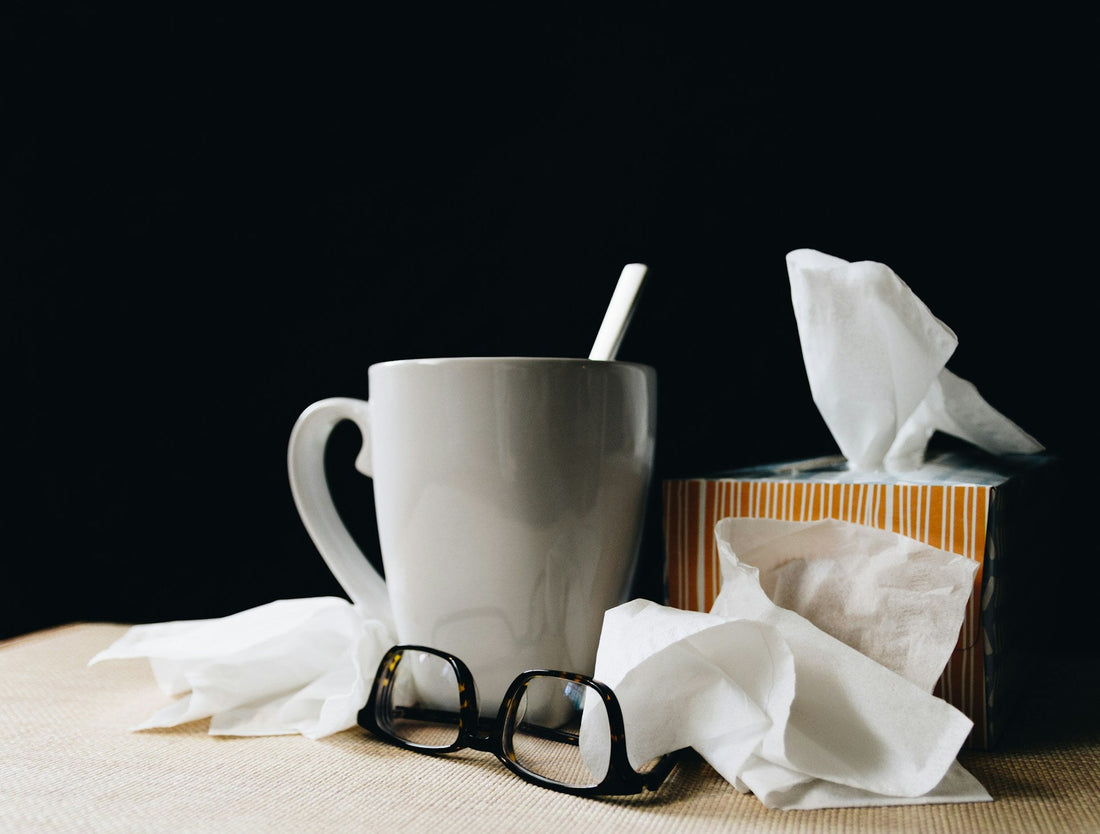 a white mug next to a box of tissues with a few used tissues on the table